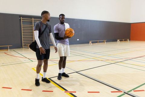 Two men talking and holding basketball on indoor gym court during casual training session