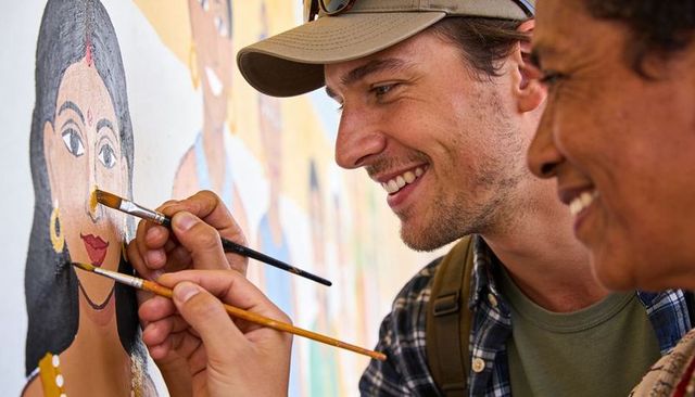 Smiling volunteers painting colorful indian portrait community mural, collaborative teamwork