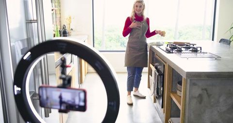 Home cook filming citrus recipe while holding lemon in modern kitchen with ring light