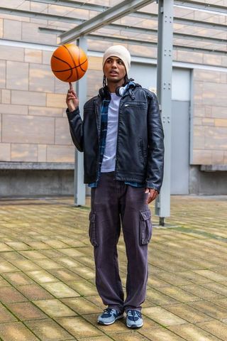 African american young man spinning basketball on finger in urban courtyard with headphones