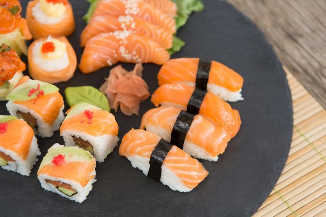 Slate tray of assorted sushi kept on mat against wooden background