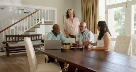 Senior group discussing plans using laptop and documents at home