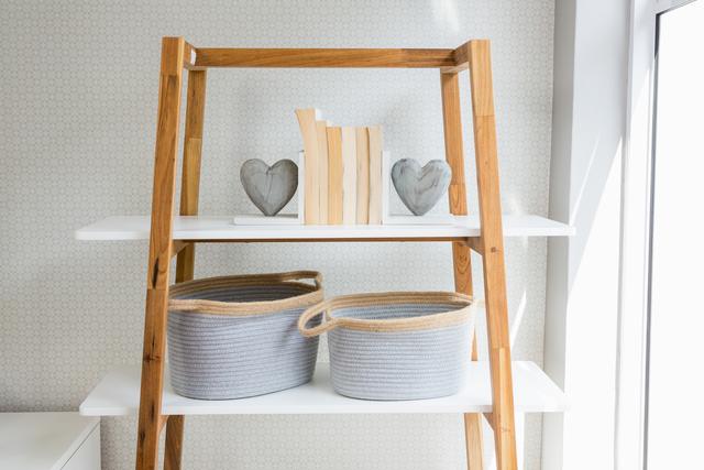 Modern wooden shelf in a bright living room featuring neatly arranged books, heart-shaped decor, and woven baskets. Ideal for articles or advertisements on home organization, interior design, minimalist living, and stylish home decor solutions.