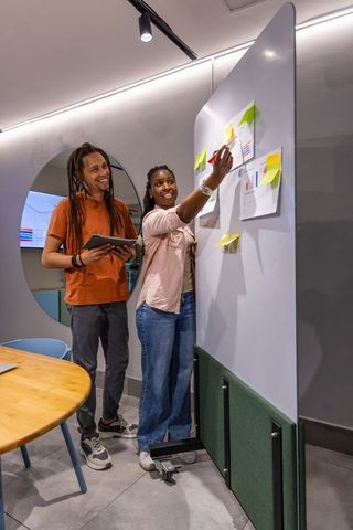 African american team brainstorming with sticky notes on mobile board in modern office