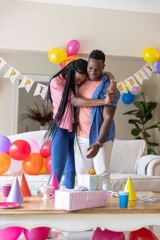 African american couple hugging celebrating birthday at home with balloons and gifts