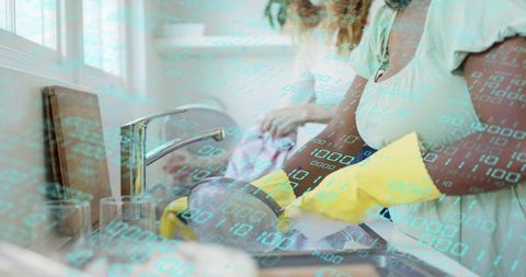 Woman washing dishes wearing yellow gloves while partner drying in sunlit kitchen, data overlay