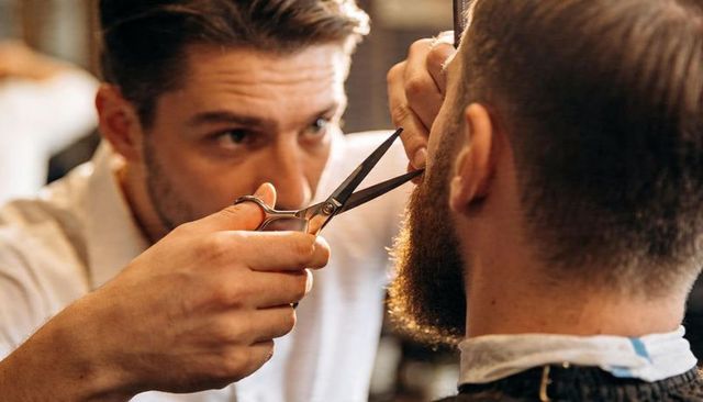 Barber trimming client's beard with scissors closeup precision grooming studio lighting