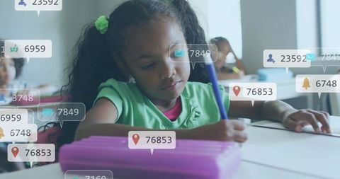 Young schoolgirl writing in classroom with floating social media notification overlays