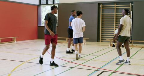 Multiracial basketball team helping teammate up and regrouping during indoor court drills