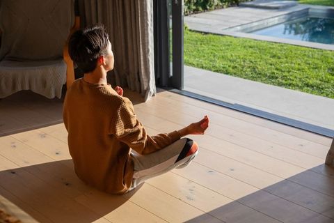 Asian man meditating by sliding glass door with morning sunlight and backyard pool wellness