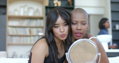 Two friends leaning together puckering lips while checking makeup at home vanity mirror