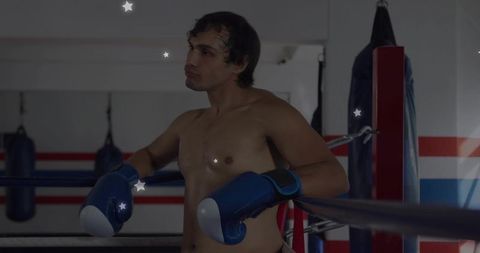 Shirtless boxer leaning on ring ropes wearing blue gloves showing focus and stamina