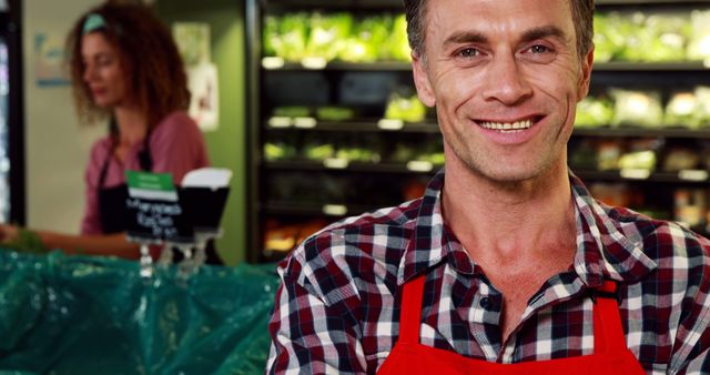 Smiling Grocery Store Worker in Red Apron in Produce Section - Download Free Stock Images Pikwizard.com