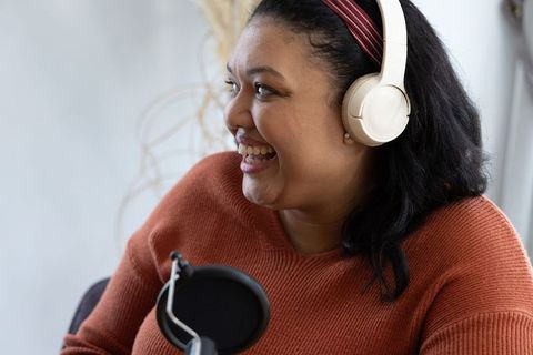 Asian woman smiling speaking into microphone wearing white headphones and maroon headband