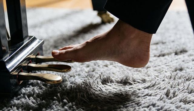 Bare foot pressing piano pedal on plush gray rug closeup showing intimate music moment