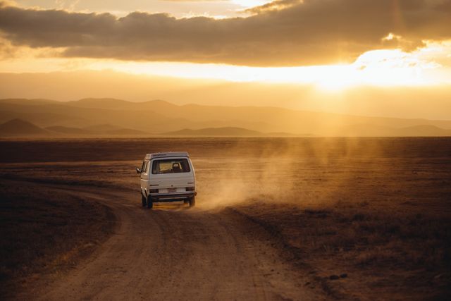 The van is driving on a dusty road during sunset in a vast desert landscape. This image captures the essence of adventure, freedom, and journey. It conveys a sense of limitless exploration and can be used for travel websites, adventure blogs, road trip advertisements, or inspirational content emphasizing open roads and natural beauty.