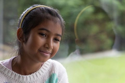 Indian girl gazing reflectively by window wearing cream knit sweater and yellow headband