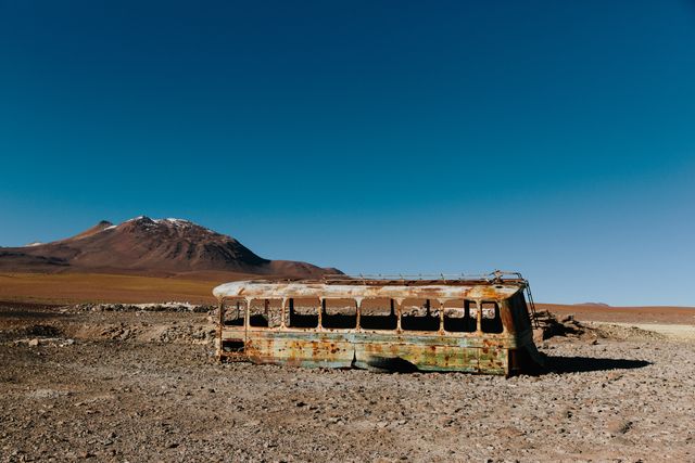 Depicts an old, rusted bus abandoned in a remote desert with mountains in the background. The scene evokes feelings of isolation and tranquility. Ideal for use in travel blogs, adventure magazines, graphic design projects, and articles about abandoned places or historical decay.