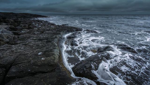 Waves washing rugged bedrock and tidal channels foam-tracing moody overcast rocky coastline