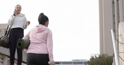 Mature women climbing urban stairs carrying yoga mat, coffee and smartphone