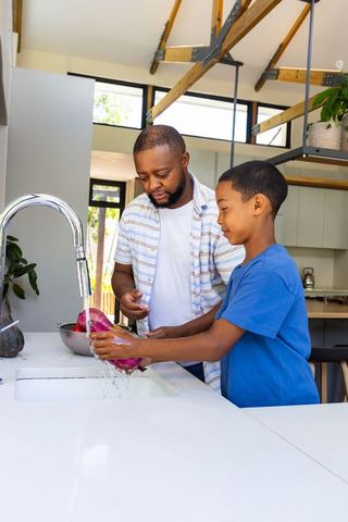 African american father teaching son to wash purple vegetables at modern kitchen island