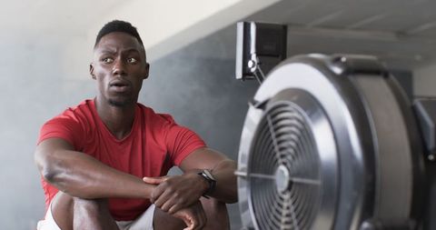 Athletic man resting by rowing machine in modern gym environment