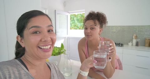 Smiling diverse women toasting with water glasses in bright modern kitchen