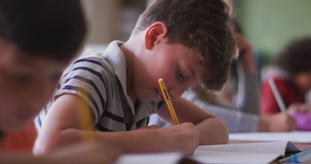 Caucasian boy sitting at desk and writing in notebook in elementary school class - Download Free Stock Photos Pikwizard.com
