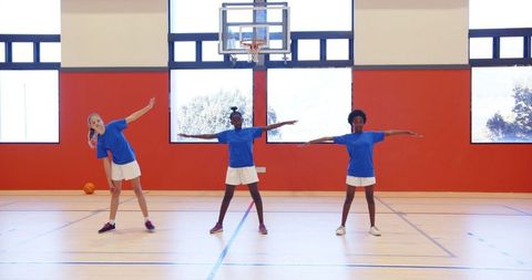 Youth Athletes Stretching in Gym with Basketball Hoop