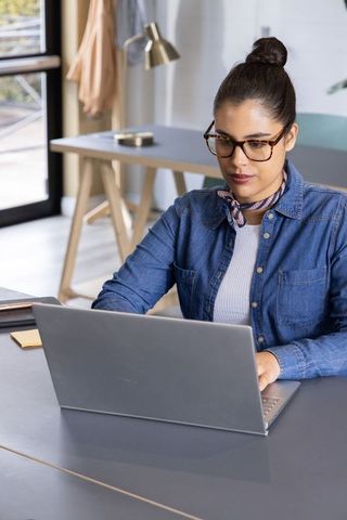 Young woman working on laptop in modern home office with tortoiseshell glasses