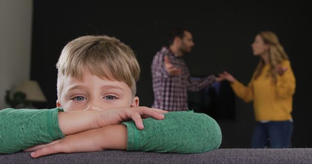 Boy resting his head on a couch, looking sad as his parents argue in the background. Useful for illustrating family conflict, child distress due to domestic issues, and the emotional impact on children. Can be used in articles, blog posts, or informational materials related to family dynamics, mental health, and conflict resolution.