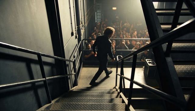 Performer descending metal staircase toward crowded stage barrier backstage spotlight