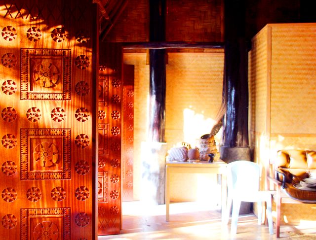 Sunlight streaming into traditional wooden house with eclectic decor. Features include wooden walls with ethnic patterns, rustic style, homey elements and natural light. Ideal for showcasing cultural heritage, rustic interior design, and warm home environments.