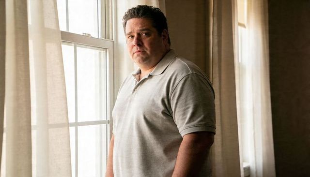 Contemplative man standing by window wearing light gray polo, natural light home interior