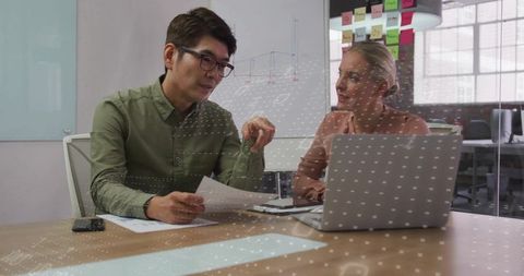Colleagues collaborating on project, man pointing at documents while woman using laptop