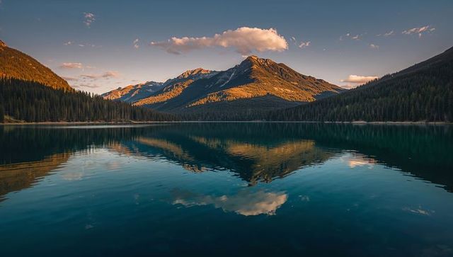 Sunlit mountain peak reflecting on calm turquoise alpine lake at golden hour