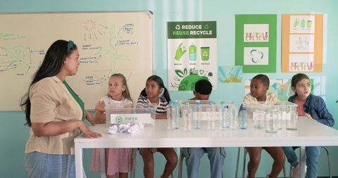 Teacher leading recycling workshop with diverse children sorting bottles and paper