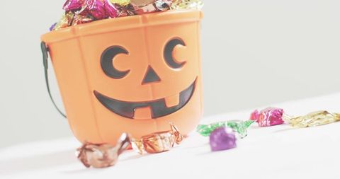 Spilling halloween candy from jack-o-lantern bucket on white background, copy space