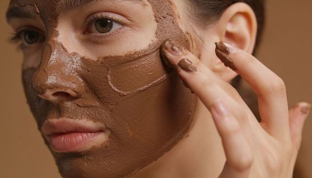 Closeup woman applying brown clay facial mask with fingers skincare spa ritual