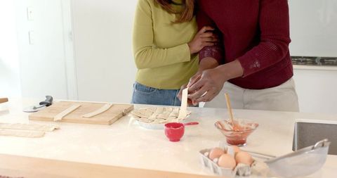 Diverse couple weaving lattice pie crust together on bright modern kitchen counter