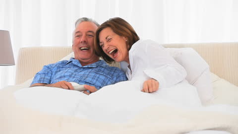 Mature Couple Relaxing in Bed While Watching TV