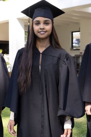 Proud graduate in cap and gown standing in university garden