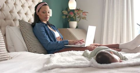 Hispanic Mother Multitasking on Laptop in Cozy Bedroom