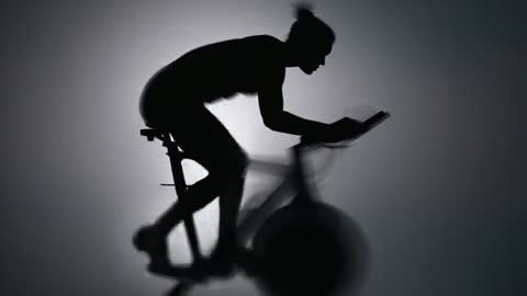 Female cyclist silhouette pedaling intensely on indoor spin bike capturing dynamic motion