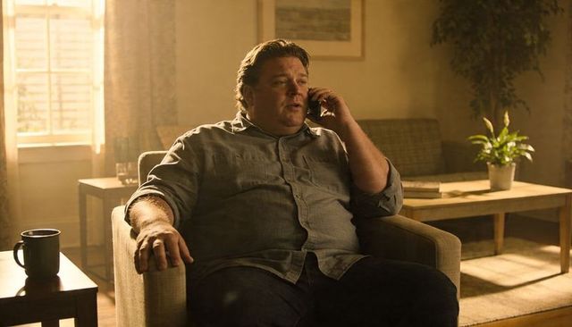Middle-aged man talking on smartphone while relaxing in cozy living room armchair with coffee mug