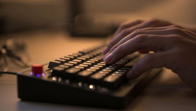Adult hands typing on compact mechanical keyboard with red knob and blue LED lighting