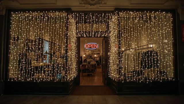 Glowing boutique storefront with curtain string lights and neon open sign at night, cozy