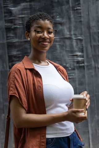 Confident african woman holding takeaway coffee, smiling, glasses and casual street style