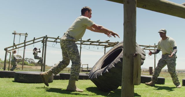 Fit caucasian male soldier in army fatigues flipping tractor tyre on army obstacle course in the sun. healthy active lifestyle, cross training outdoors at boot camp.