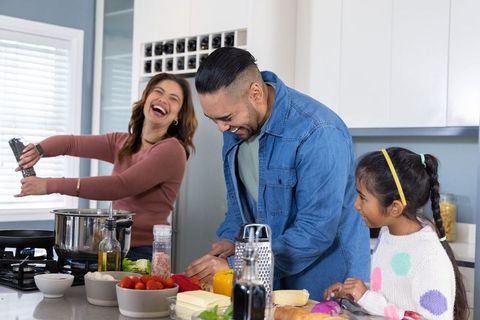 Diverse family cooking together in modern kitchen, father chopping vegetables, mother seasoning